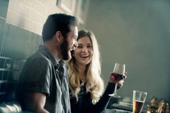 miling couple sharing wine and laughter at a bar, the emotional connection that counters common marriage warning signs
