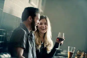 miling couple sharing wine and laughter at a bar, the emotional connection that counters common marriage warning signs