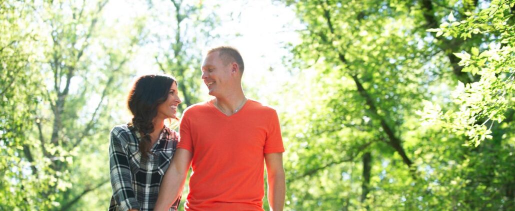 EFT vs Gottman Method: a smiling couple walking hand in hand on a sunlit wooded path